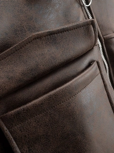 Macro detail of dark brown faux leather pilot jacket showing pocket seams and silver zipper