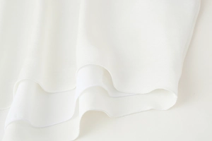 Détail du tissu en satin de soie blanc avec ourlet roulé et design drapé multicouche