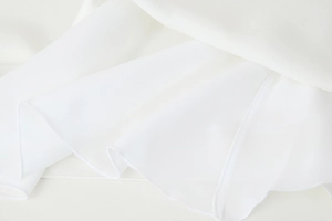 Vue détaillée du tissu en satin blanc avec ourlet à volants et coutures de haute qualité