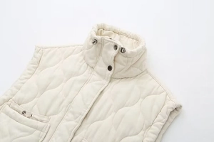 Close-up of beige quilted vest featuring high stand collar with black drawstring toggles