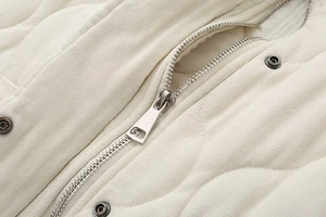 Close-up of ivory quilted vest featuring a silver metal zipper and snap button details