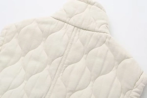 Detailed view of the wavy quilted stitching and stand-up collar on the beige vest jacket