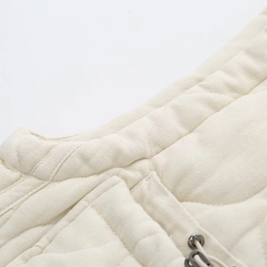 Detailed macro view of cream quilted vest showing fine twill texture and metal cord adjuster