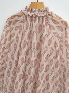 Detail of high neck ruffle and metallic paisley print on pleated long sleeve shirt