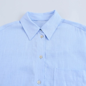 Détail du col d'une chemise bleu clair avec boutons nacrés et texture de tissu tissé