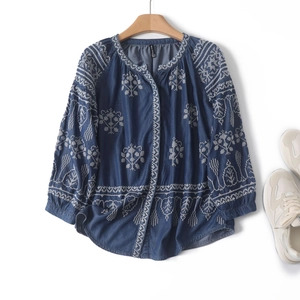 Detail of white ethnic floral embroidery on navy blue long-sleeved boho blouse