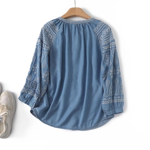 Detail view of white flower embroidery and wavy patterns on light blue long sleeve shirt