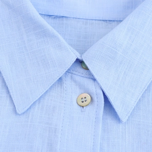 Détail d'un col de chemise en coton-lin bleu clair avec des boutons en nacre irisante