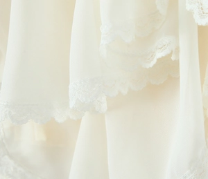 Detail of cream chiffon fabric with delicate lace patchwork and wavy scalloped edges