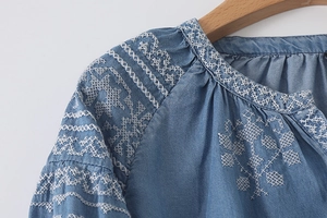 Detail of white geometric embroidery on light blue chambray shirt with pleated neckline