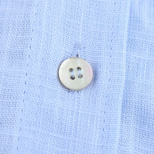 Détail d'un bouton en nacre naturelle sur le tissu en lin bleu clair respirant
