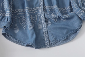 Detail of white floral embroidery on blue denim shirt with a curved hemline and soft texture