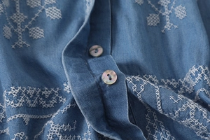Close-up of floral embroidery on light blue denim shirt with iridescent pearl buttons