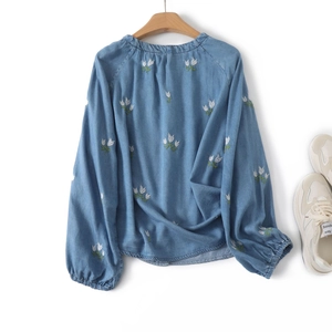 Détail d'un chemisier bleu clair à manches longues avec broderie tulipe et col rond élégant