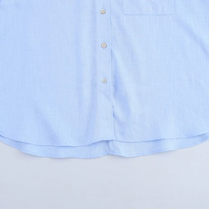 Détail d'une chemise en lin bleu clair avec patte de boutonnage, poche et ourlet arrondi