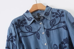 Détail de la chemise en jean bleu clair avec broderie florale et boutons texturés blancs