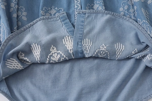 Detailed white flower embroidery on light blue denim fabric hem with precision stitching