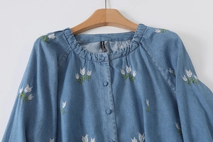 Détail de broderie de tulipes blanches sur un chemisier bleu clair à col rond