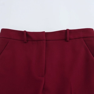Detail van bordeauxrode uitlopende broek met stoftextuur, riemlussen en zijzakken