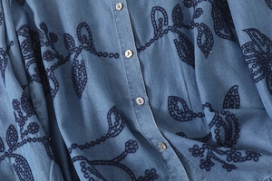 Détail de la broderie florale sur chemise bleue avec boutons en nacre