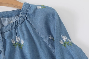 Détail de la broderie florale et du col plissé sur cette blouse en jean bleu clair