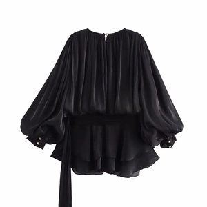 Detail of elegant black pleated mini dress showing satin texture and pearl cuff buttons