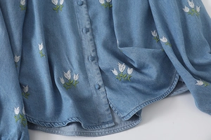 Détail de la chemise en jean bleu montrant la broderie de tulipes et boutons en tissu