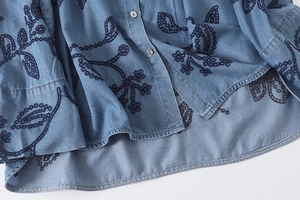Détails de la chemise en jean bleu avec broderie florale et boutons en nacre de perle
