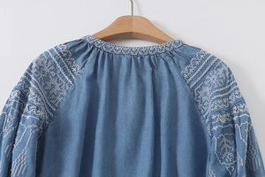Detail of white floral embroidery on blue denim round neck long sleeve shirt