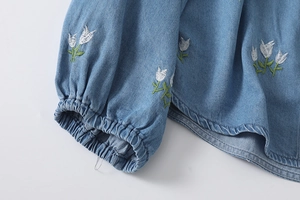 Gros plan détaillé d'une chemise en jean bleu clair avec broderie de tulipes blanches sur manches
