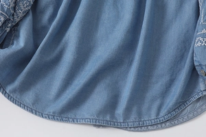Detailed close-up of white wavy embroidery on blue denim long sleeve shirt hem
