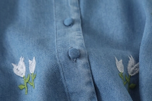 Détail de broderie tulipe fleurie et boutons recouverts sur une chemise en jean bleu