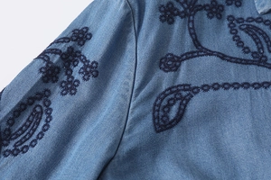 Gros plan détaillé d'une broderie fleurie bleu marine sur l'épaule d'une chemise en jean