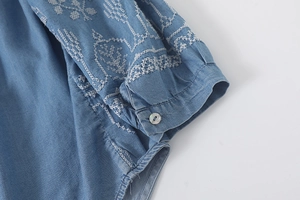 Detail of floral cross-stitch embroidery and mother-of-pearl button on blue denim sleeve