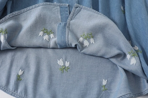 Gros plan sur les broderies délicates de fleurs blanches sur chemise en denim bleu clair