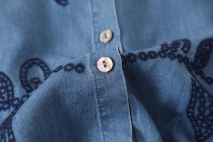 Détail d'une chemise en jean bleue avec broderie florale et boutons en nacre
