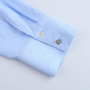 Détail macro d'un poignet de chemise en lin bleu clair avec fermeture à bouton et texture