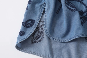 Détail de la broderie florale sur chemise en jean bleue avec coutures de qualité