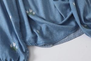 Détail de broderie florale de tulipes sur tissu denim bleu clair à texture sergée