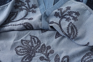 Vue détaillée de broderies florales bleues sur le tissu d'une chemise bleu clair