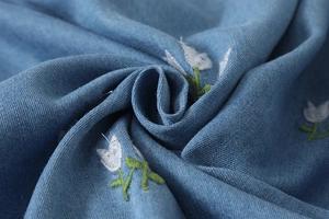 Gros plan sur tissu denim bleu avec broderie florale de tulipes blanches et sergé