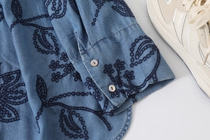 Détail de la broderie florale sur la chemise bleue à manches longues et boutons nacrés