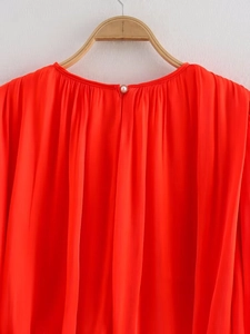 Detail of red pleated mini dress featuring a delicate pearl button back closure