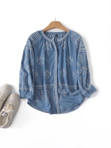 Light blue long sleeve floral embroidered shirt with white stitching on a wooden hanger