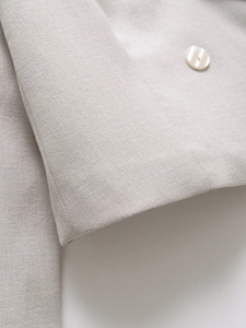 Detailaufnahme des strukturierten Stoffes und des weißen Knopfes am hellgrauen Blazer