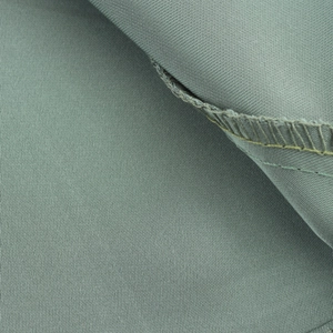 Gros plan du tissu satiné vert olive montrant le tissage sergé et la couture surjetée fine