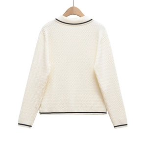 Detailed view of the waffle knit texture and black striped trim on a cream polo sweater