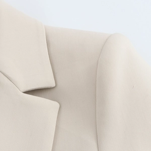 Detail of notched lapel and shoulder tailoring on a beige women's suit jacket