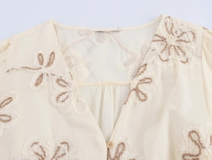 Detail of floral embroidery on a V-neck cream dress with delicate pleats and button
