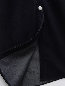Detail view of the pleated denim dress hem with silver metal button and fine stitching